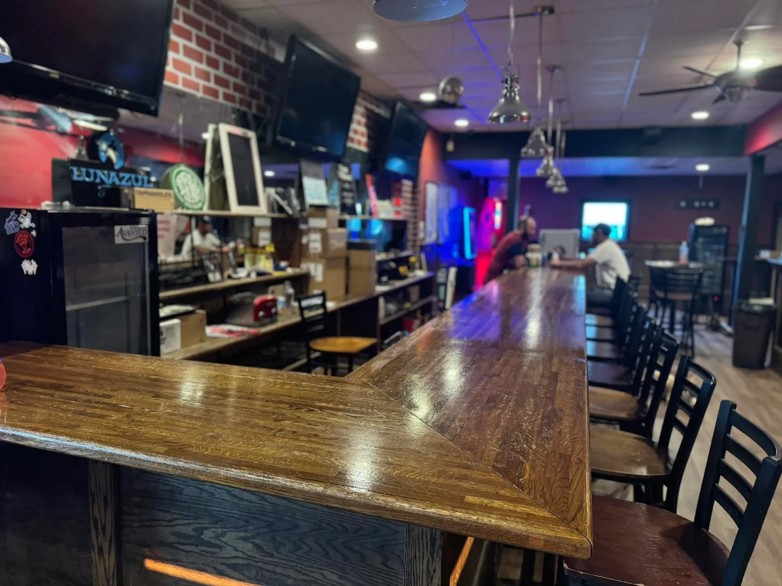 The long wooden bar on a quiet afternoon, screens above it and the back room beyond