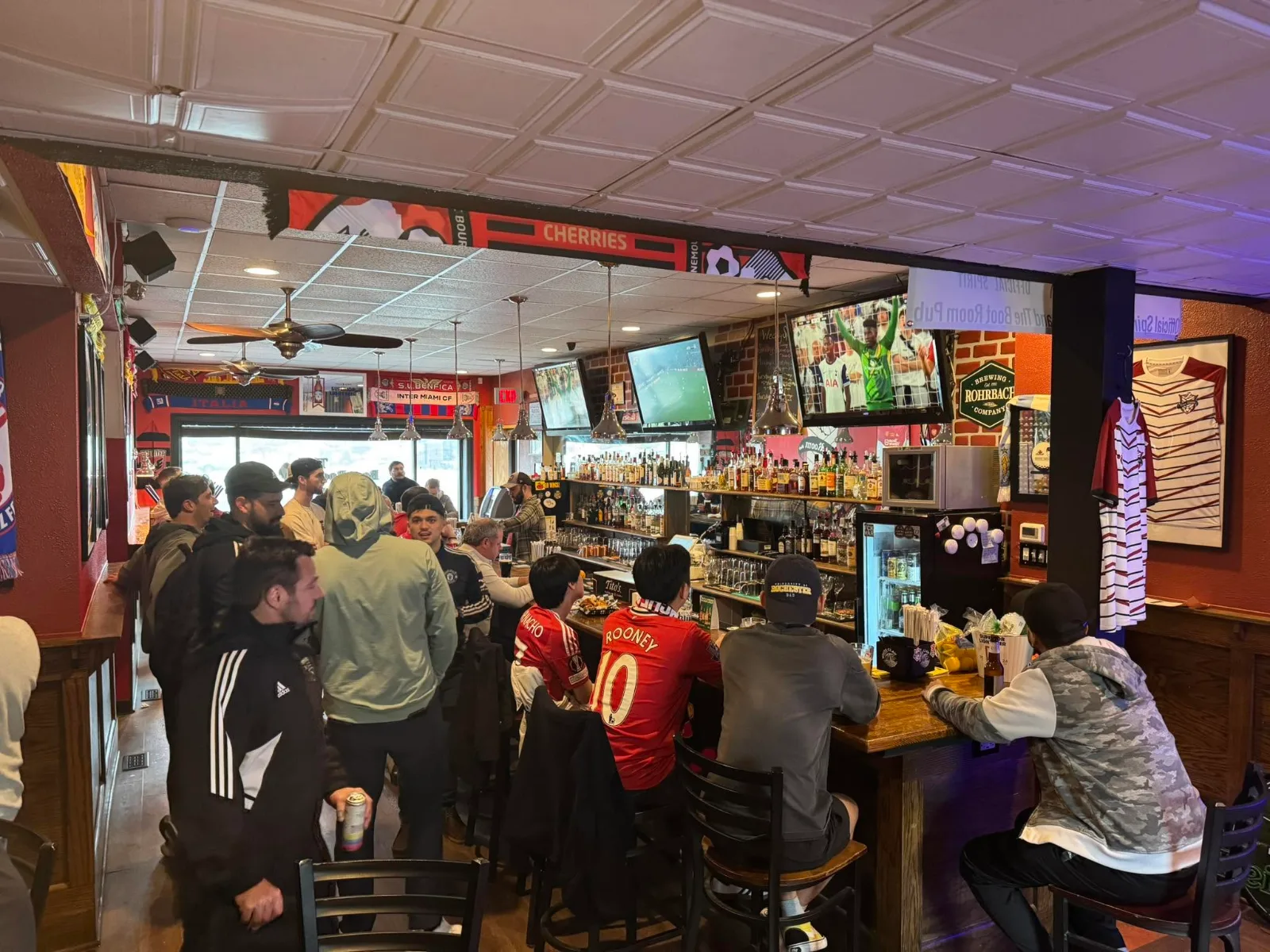 A packed bar watching soccer on several screens, club scarves hung along the beam above and two people in Manchester United shirts at the counter